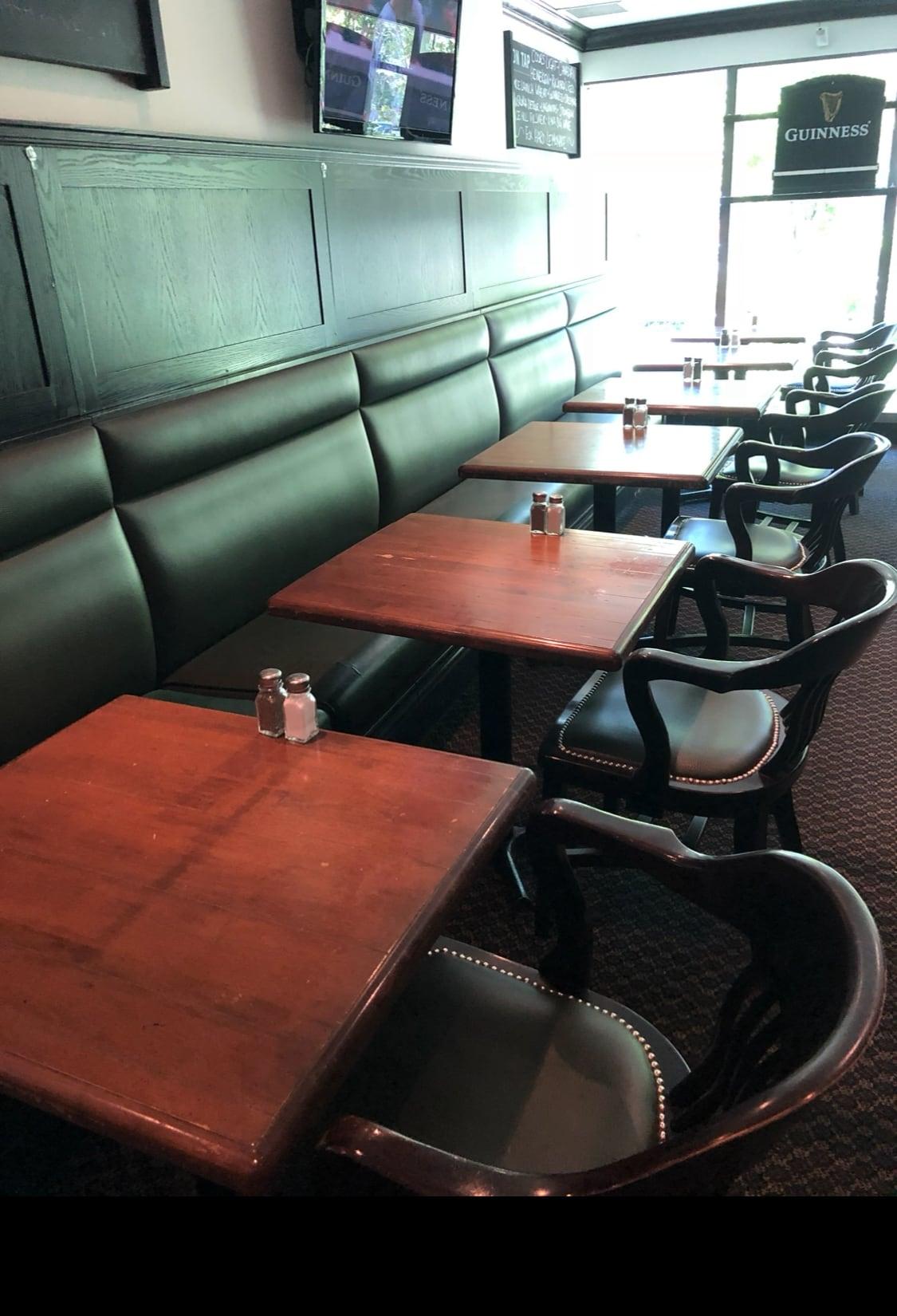 Green vinyl booth seating along a pub wall next to wood dining chairs with nailhead-trim seats