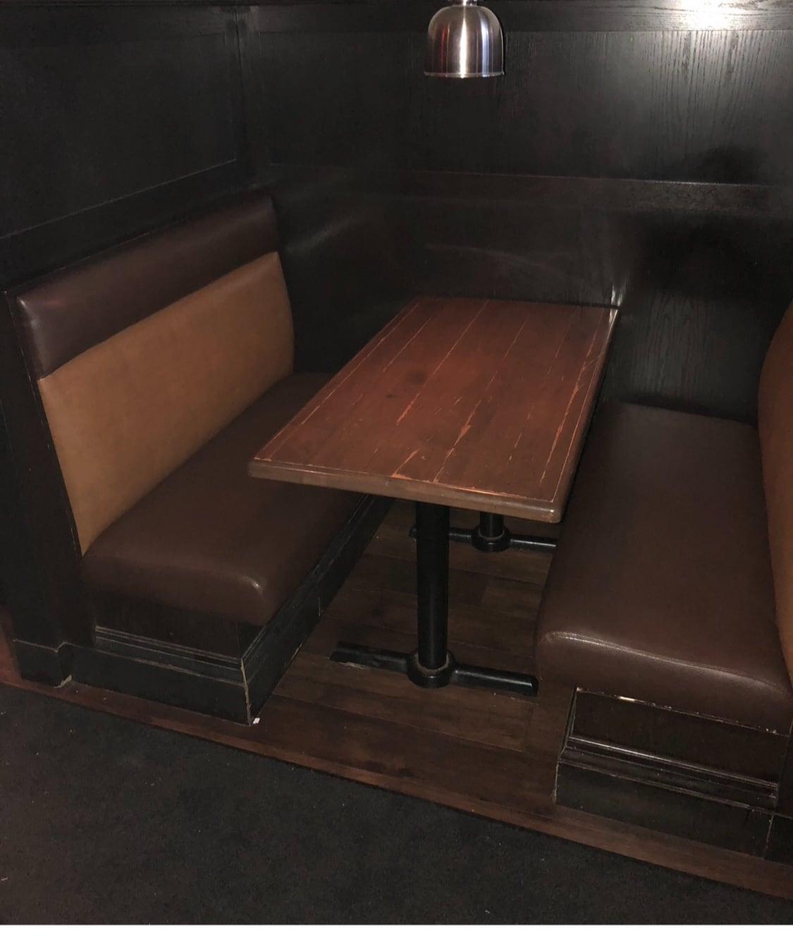Two-seat corner restaurant booth reupholstered in dark brown vinyl beside a rustic wood table