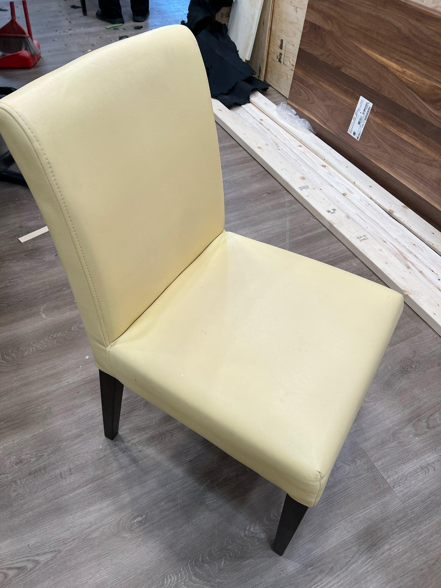 Armless dining chair reupholstered in pale yellow vinyl, photographed in the workshop
