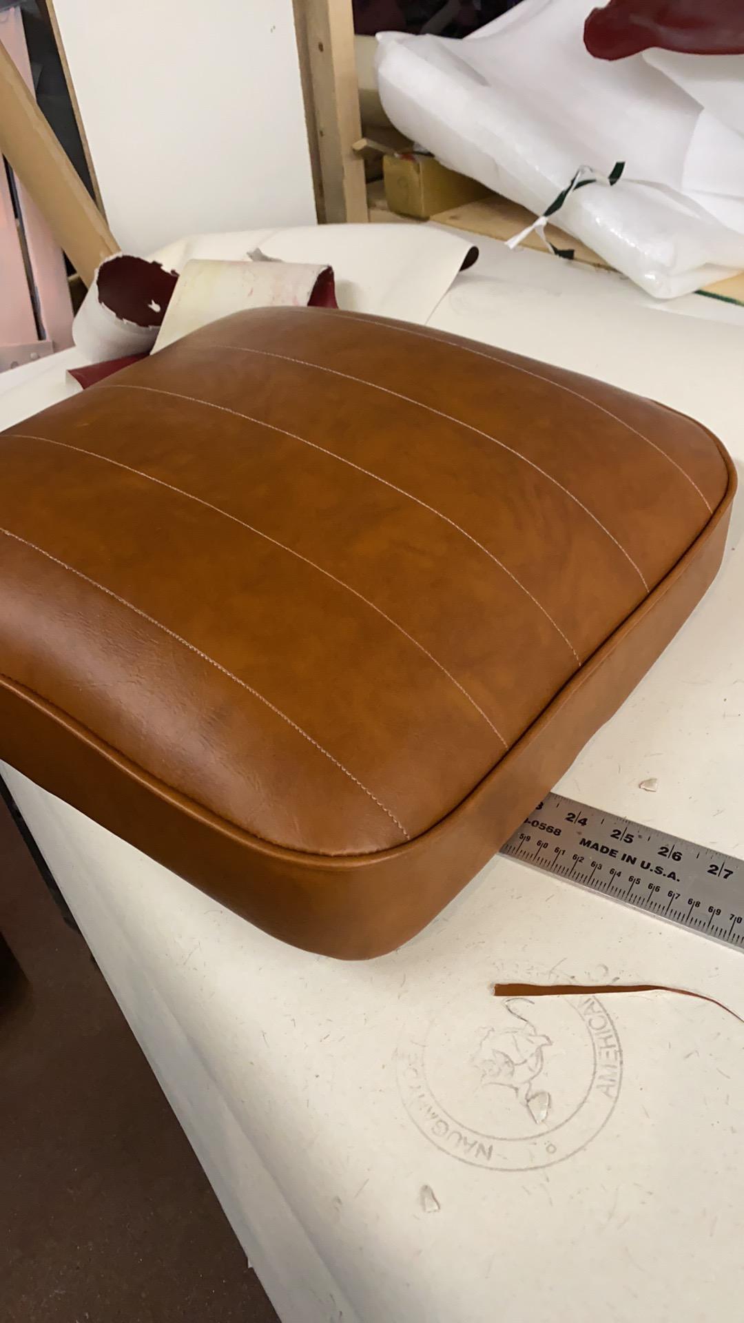 Finished tan vinyl seat cushion with channel stitching on the workshop bench